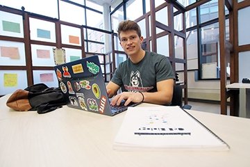 Student working on his laptop sitting at a table