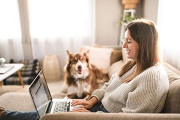 Woman using a laptop at home with with a dog nearby.