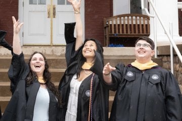 Three MSW graduates throwing their graduation caps in the air in front of Carver Hall