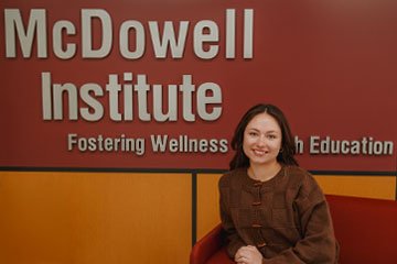Female student sitting in front of McDowell Institute signage.