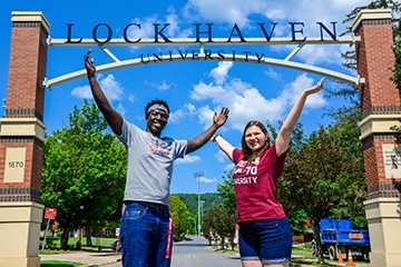 A male and female student pose with arms raised under a Lock Haven University sign