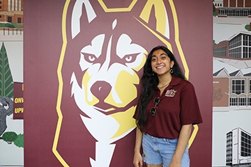 A Bloomsburg Admissions tour guide poses by a large image of Roongo - the Husky mascot