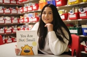 A CU Early Childhood Education major holding the book "You Are (Not) Small" in an elementary school