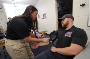 A pre-athletic training student takes blood pressure of another student in hands-on instruction in class