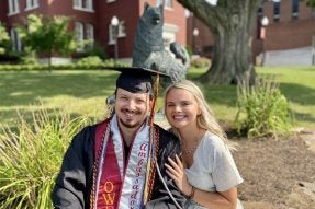 Cole Neff '20 (left) sits in front of the Husky statue with his wife.