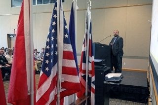 A group of flags. A man talking through a microphone in the background. 