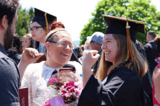 A girl celebrating graduation in a cap and gown with two other people (a male and a female).