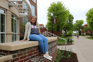 A girl sitting on a ledge in front of a building. 