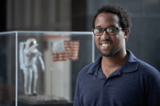 A man standing in front of an astronaut with a flag in a glass case.