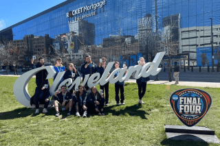 A group of people standing and sitting around a Cleveland sign. 