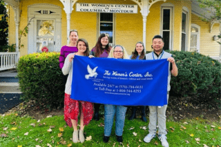 Members of the Women's Center staff stands in front of the facility with a banner.