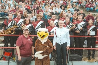 Members of the Lock Haven Marching Band pose for a photo with the Bald Eagle mascot in the stands at a football game.