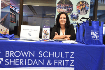 A representative from BSSF sits at a table with a blue talecloth in front of a foll up banner at the last Accounting Career Expo
