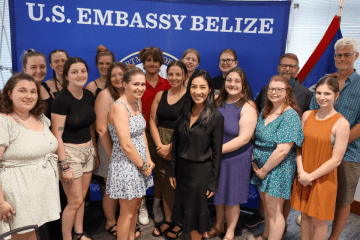 A group of students standing in front of a background that says U.S. Embassy Belize.