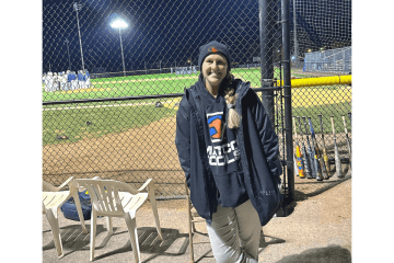 A woman standing outside the fence of a baseball field. 