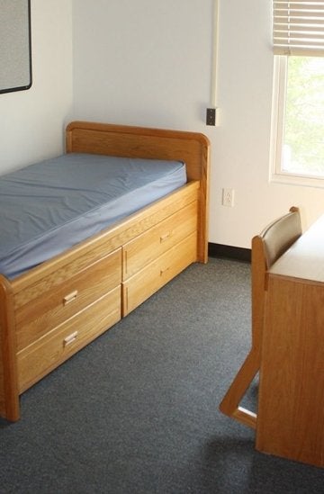 Bed with under bed storage, desk, chair and window in a bedroom of the Mount Olympus Apartments