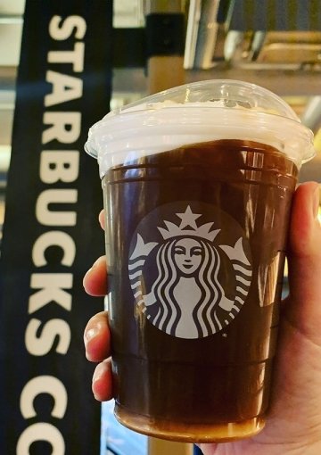 Starbucks cup being held up by a Starbucks sign.