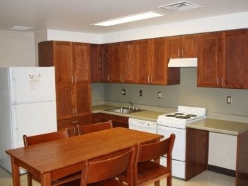 Kitchen of a Jessica Kozloff Apartment showing a table, refrigerator, range, counter space, sink and cabinets