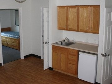 Second floor common space of Mount Olympus Apartments showing bedroom, sink, cabinets and mini fridge