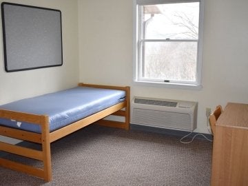 Bedroom of Montgomery Place Apartments showing bed, window, desk, chair and in wall a/c unit