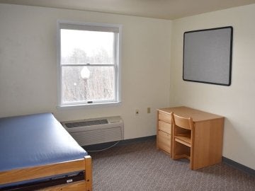 Bedroom of Montgomery Place Apartments showing bed, window, desk, chair and in wall a/c unit
