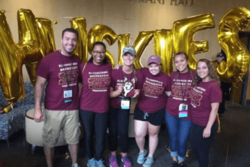 A group standing in front of gold balloons.
