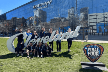 A group of people standing and sitting around a Cleveland sign. 