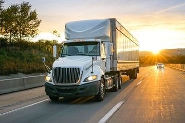 Tractor trailer driving on highway during sunset.