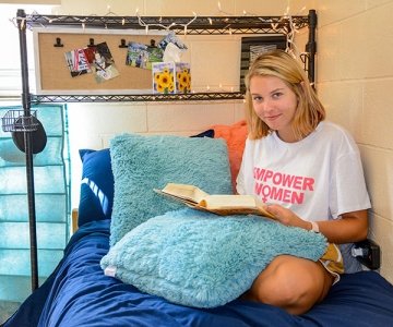Female student reading a book on a bed in Smith Hall at CU-Lock Haven