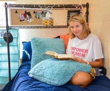 Female student reading a book on a bed in Smith Hall at CU-Lock Haven