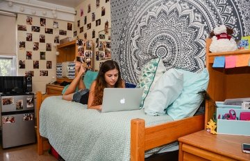 Female student using laptop while laying in bed in Smith Hall at CU-Lock Haven