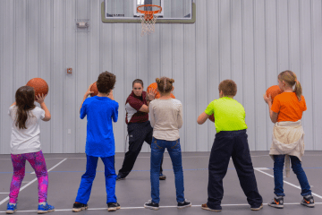 A CU-Lock Haven Health and Physical Education student leads a group of young students in a basketball drill