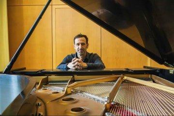 Composer Mark Olivieri seated by the piano