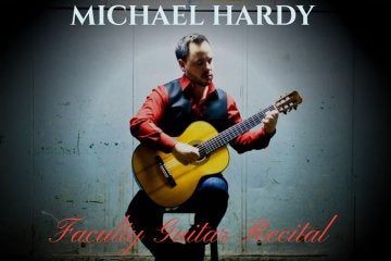 Michael Hardy sitting on a stool holding a guitar.