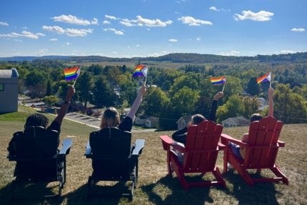Several students sit in Adirondack chairs on Laurel Lawn waving pride flags.
