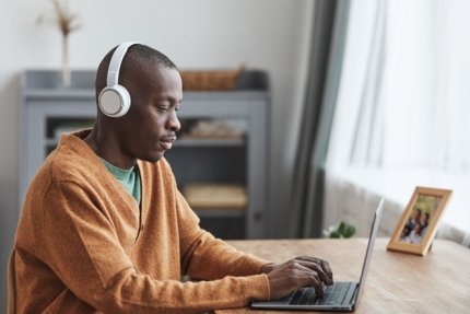 Black male adult learner wearing headphones and using a laptop.