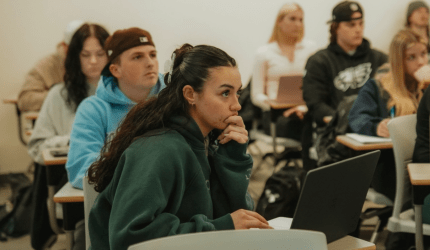 Attentive students are sitting at desks in a classroom listening to a lecture.