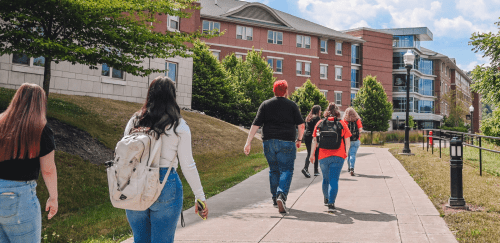 Students walk together on campus with a residence hall in the background