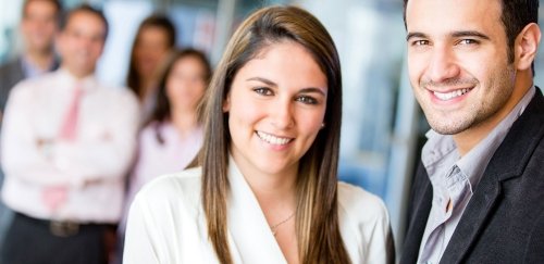 Man and woman standing together with other people blurred out in the background.