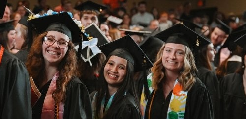 Three graduates are smiling at the 2024 Mansfield May Commencement Ceremony. 