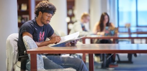Student wearing Mansfield shirt studies in library.