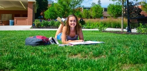Girl laying down in the grass, studying at CU-Lock Haven