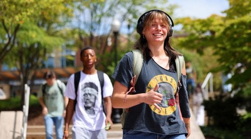 Female student wearing headphones and a Guns N' Roses t-shirt walking on a path.
