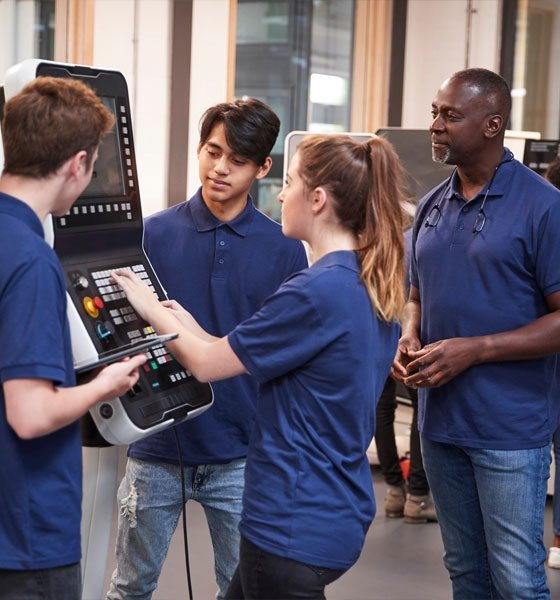 Female student programs CNC machine while two male students and trainer look on.