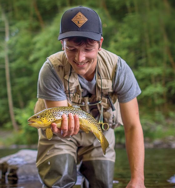 Student holding fish in a stream.