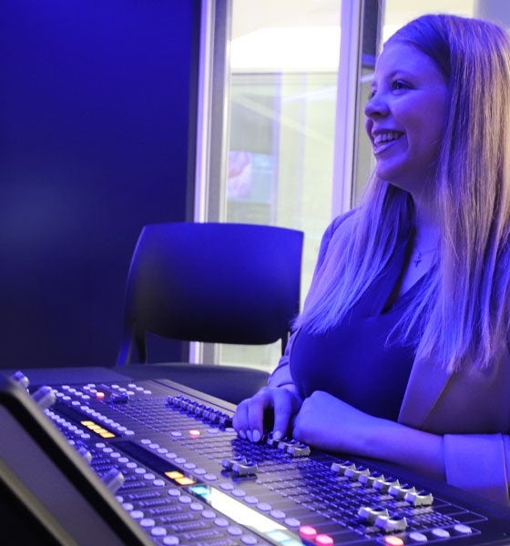Female student in dimly lit television studio control room.