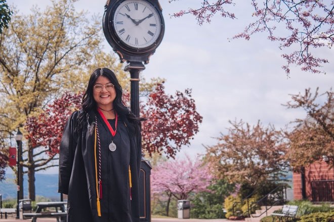 A Mansfield graduate smiles near a clock on campus