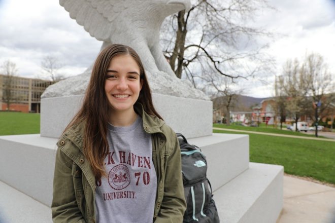 An LHU student smiles while sitting at the base of the Bald Eagle statue on campus