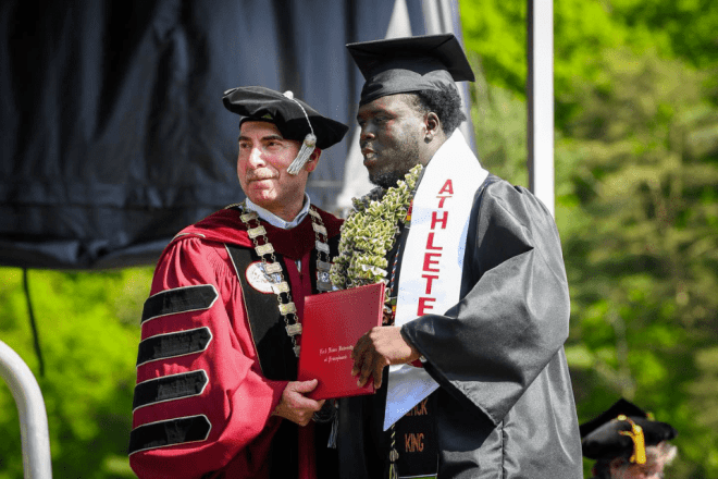 Two people standing on a stage, both holding a diploma. 
