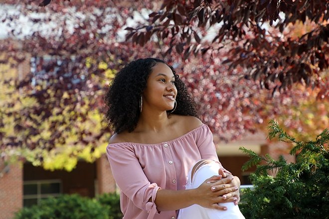 Serenity Vidot '23 smiling outside under a blooming tree.